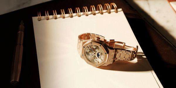 Luxury gold wristwatch on a spiral notebook in warm light.