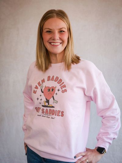 Smiling woman in a pink sweatshirt with a heart graphic.