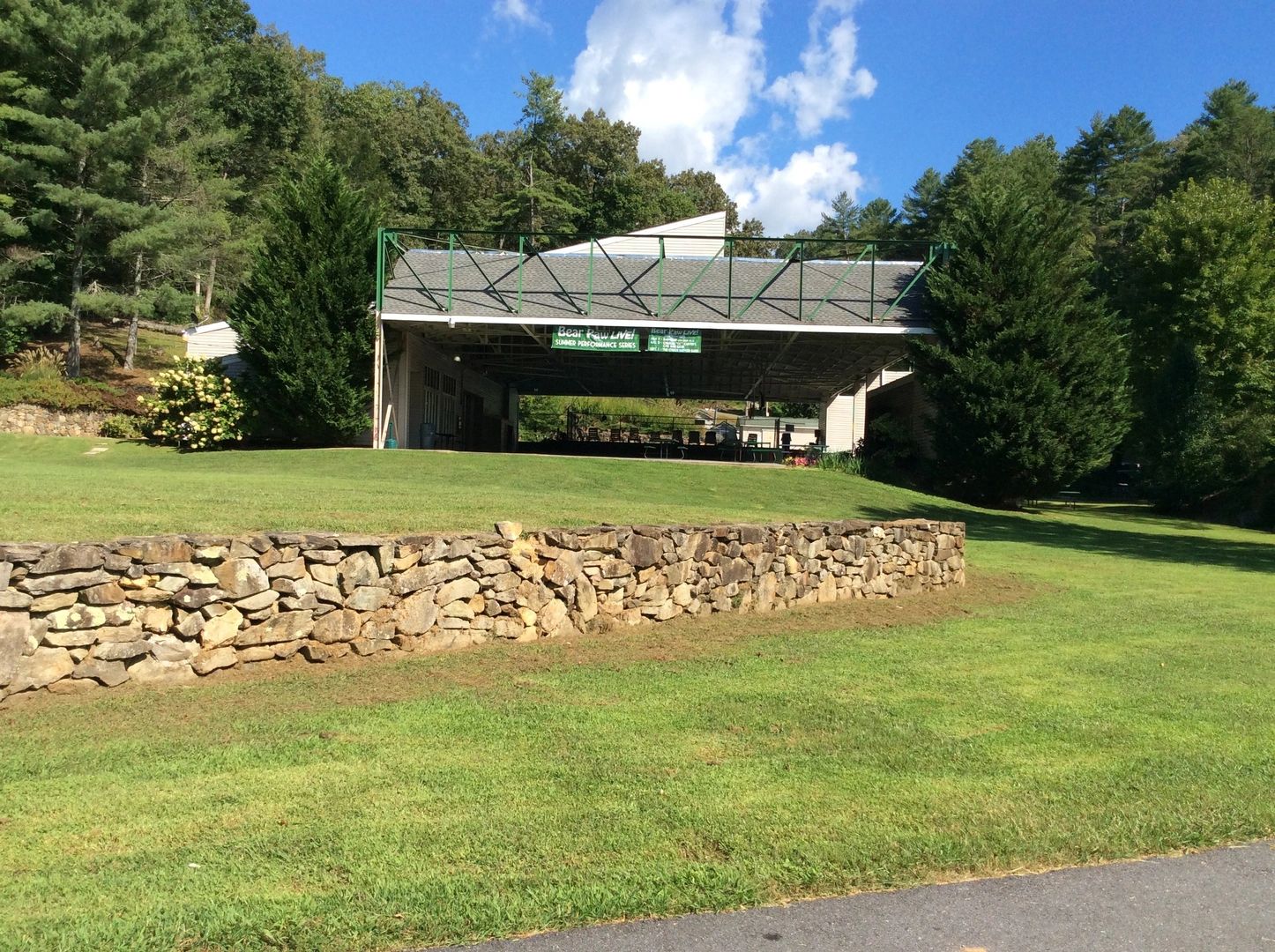 Outdoor pavilion with stone wall and green lawn under a blue sky.
