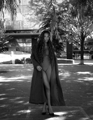 Woman confidently posing outdoors in a long coat and bodysuit.