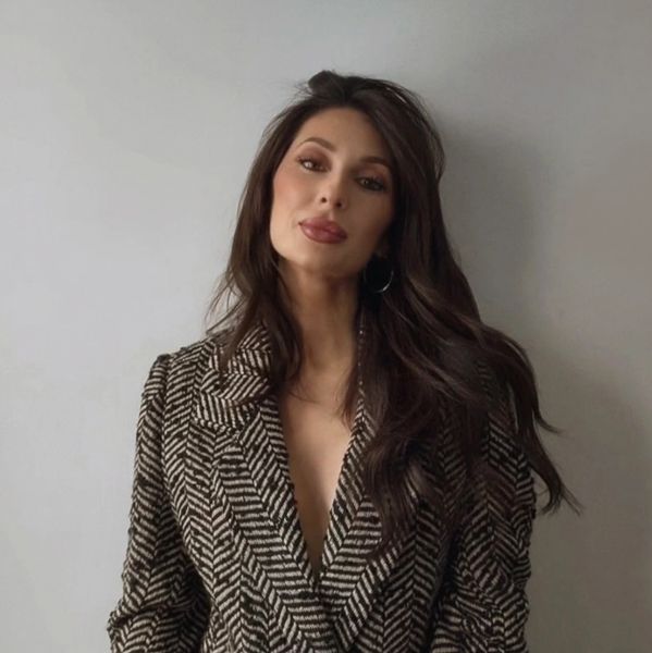 Woman with long dark hair in a patterned blazer against a plain background.