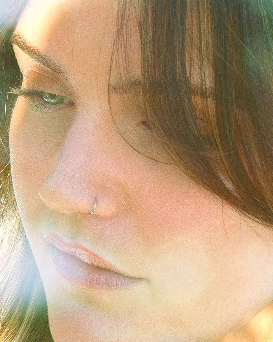 Close-up of a woman with a nose ring in soft natural light.