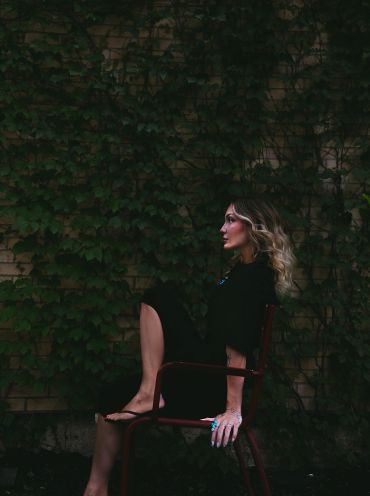 Woman sitting on a chair against a leafy wall.