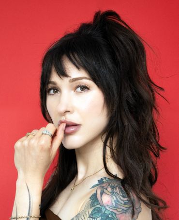 Woman with black hair and rose tattoo against a red background.