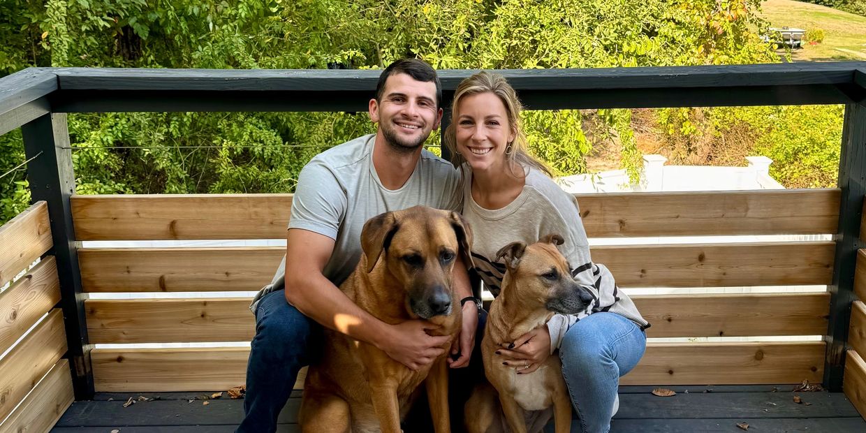 two people sitting with two dogs in front of them on a wooden deck