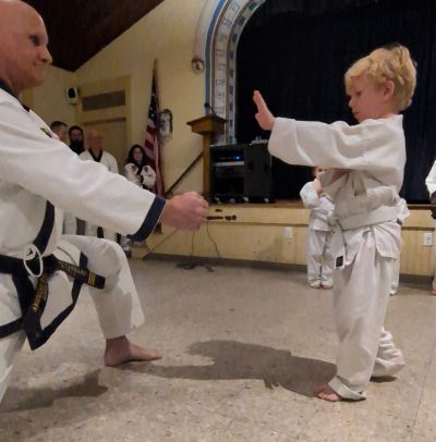 A young boy in a karate uniform prepares to break a board held by an instructor.
