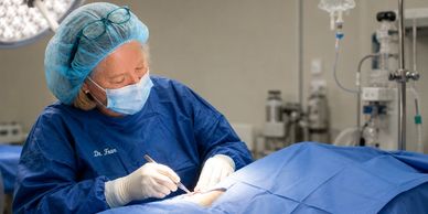 Surgeon in blue scrubs performing surgery in an operating room.
