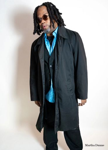 DJ Ozno rocks a black trench coat, adding a suave touch to his vest, dress shirt, and t-shirt combo.
