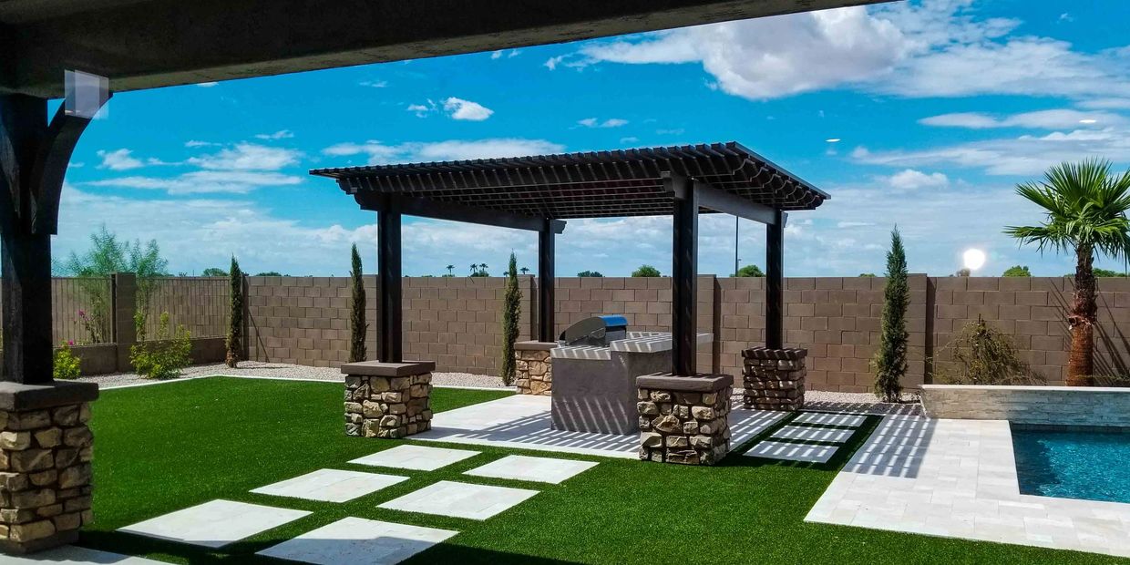 Backyard pergola with grill and pool under blue sky.