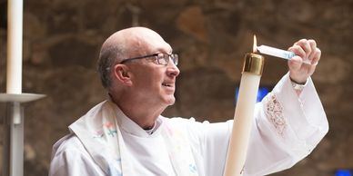 A priest lighting a candle with a joyful expression.