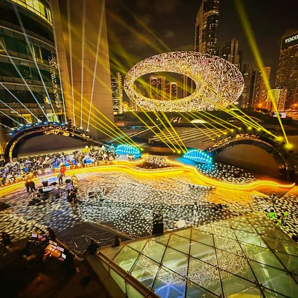 Nighttime event with illuminated calligraphy sculpture and vibrant light beams.