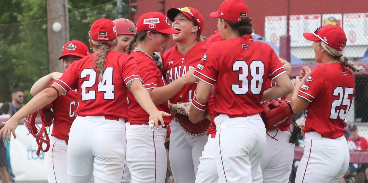 Canadian women's baseball team celebrating on the field in red and white uniforms.