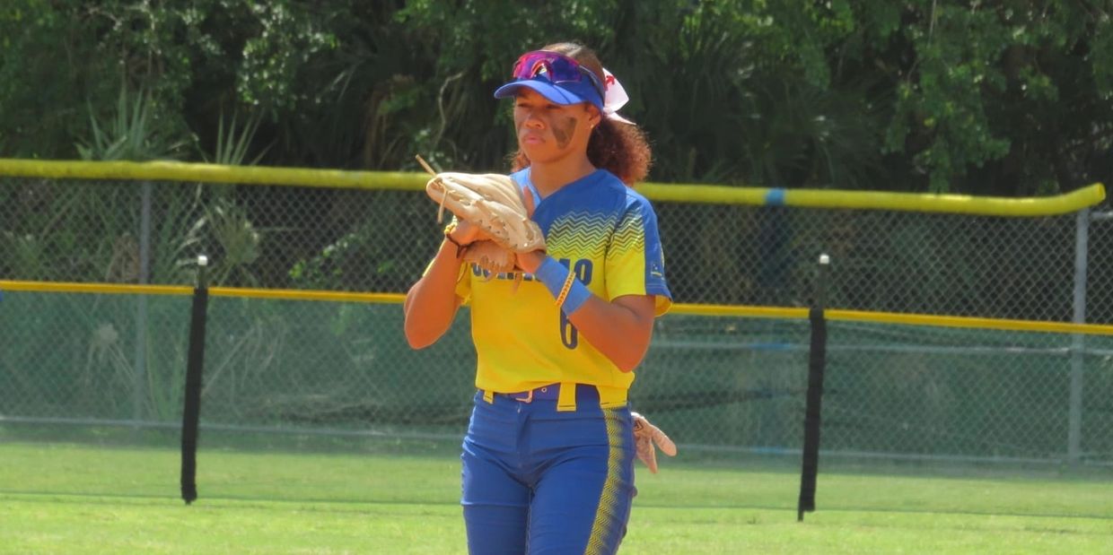 Young female softball player in yellow and blue uniform preparing to pitch.