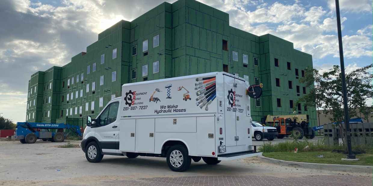 Service van parked near a construction site with a green building.