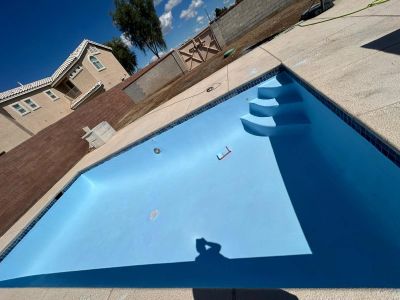 Empty backyard pool with steps and clear blue sky.