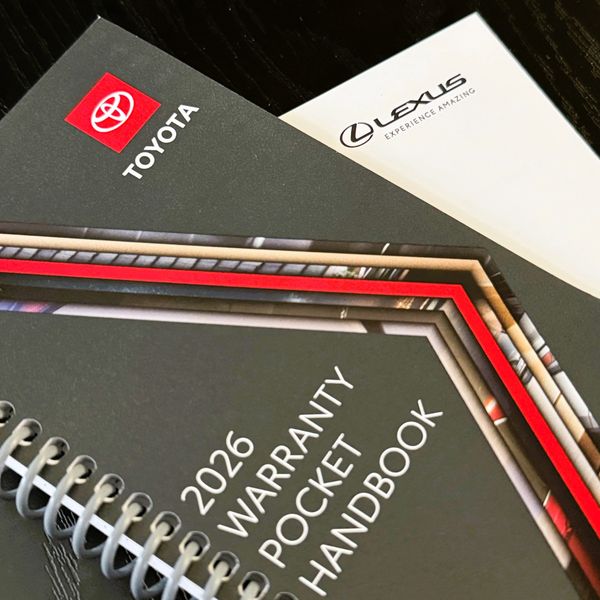 2026 Toyota warranty pocket handbook and Lexus brochure on a dark surface.