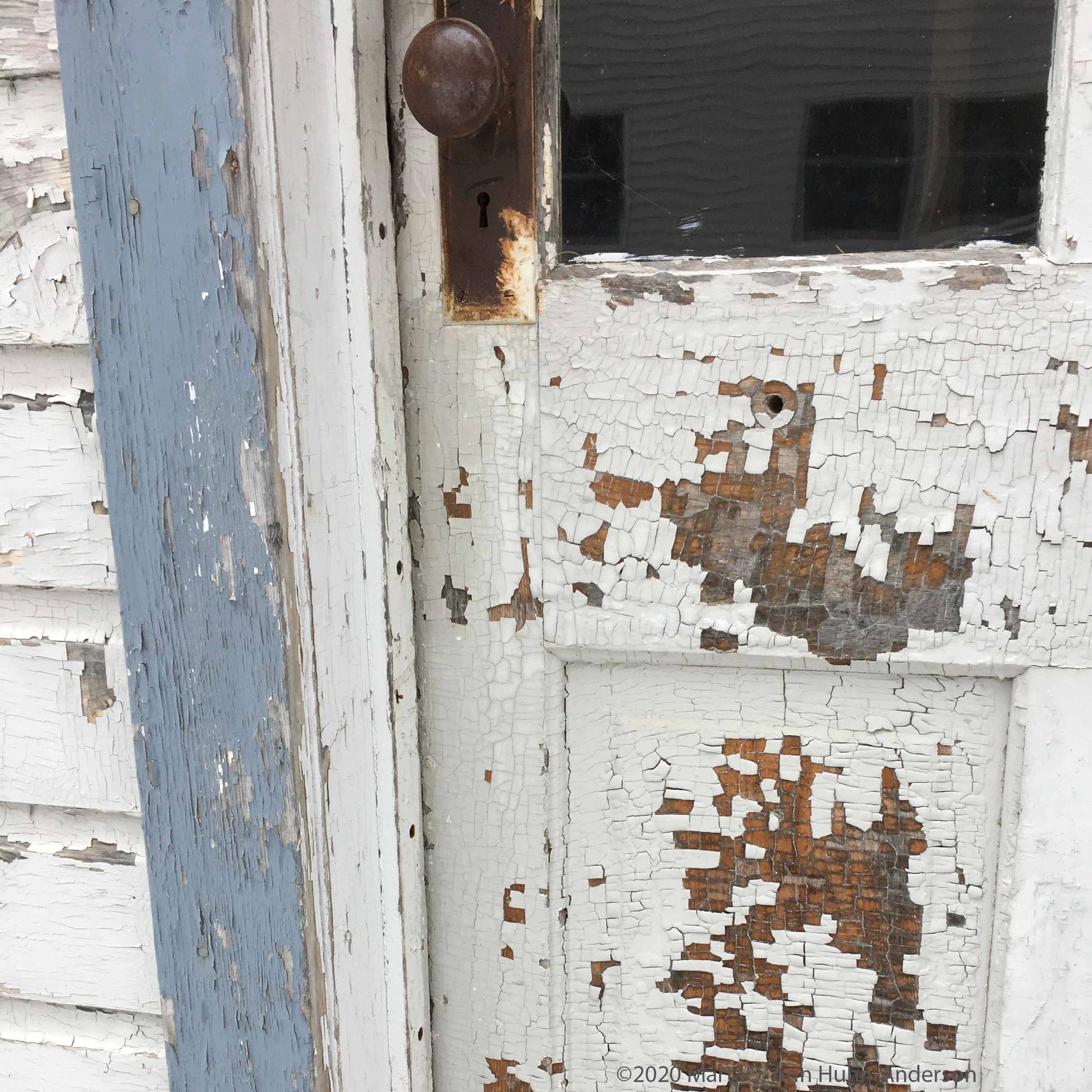 Close-up of an old, weathered door with peeling paint and a rusty doorknob.