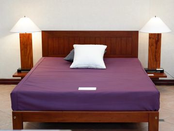 A wooden bed with a purple sheet and two bedside lamps.