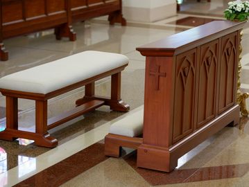 Wooden kneeling bench with cushioned seat and ornate design in a church.