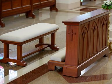 A wooden kneeler with a cross in a church interior.