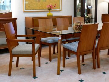 Elegant wooden dining table set with glass top and cushioned chairs.
