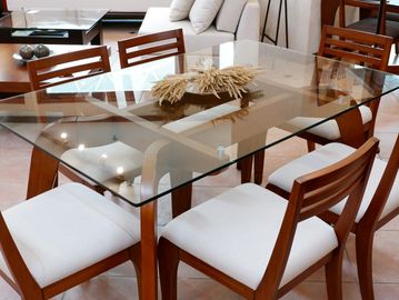 Modern glass dining table with wooden chairs and white cushions.
