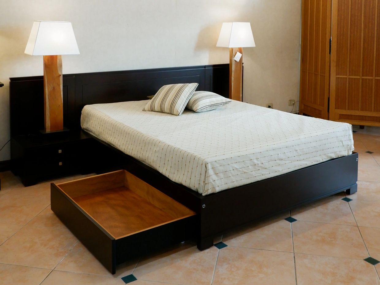 Modern bedroom with a dark wooden bed, two lamps, and an open under-bed drawer.