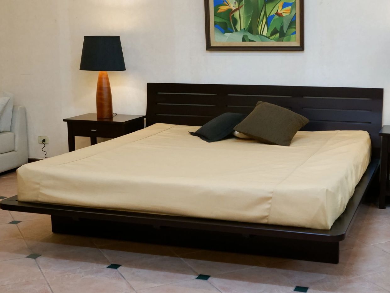 Modern bedroom with a dark wood bed, beige bedding, and a black lampshade on a wooden nightstand.