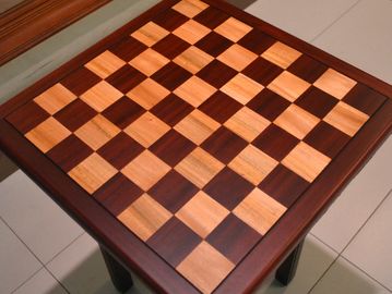Wooden chessboard with alternating light and dark squares on a table.