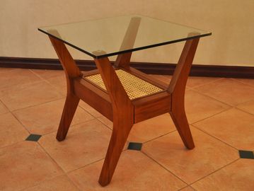 Wooden side table with glass top and woven shelf below.