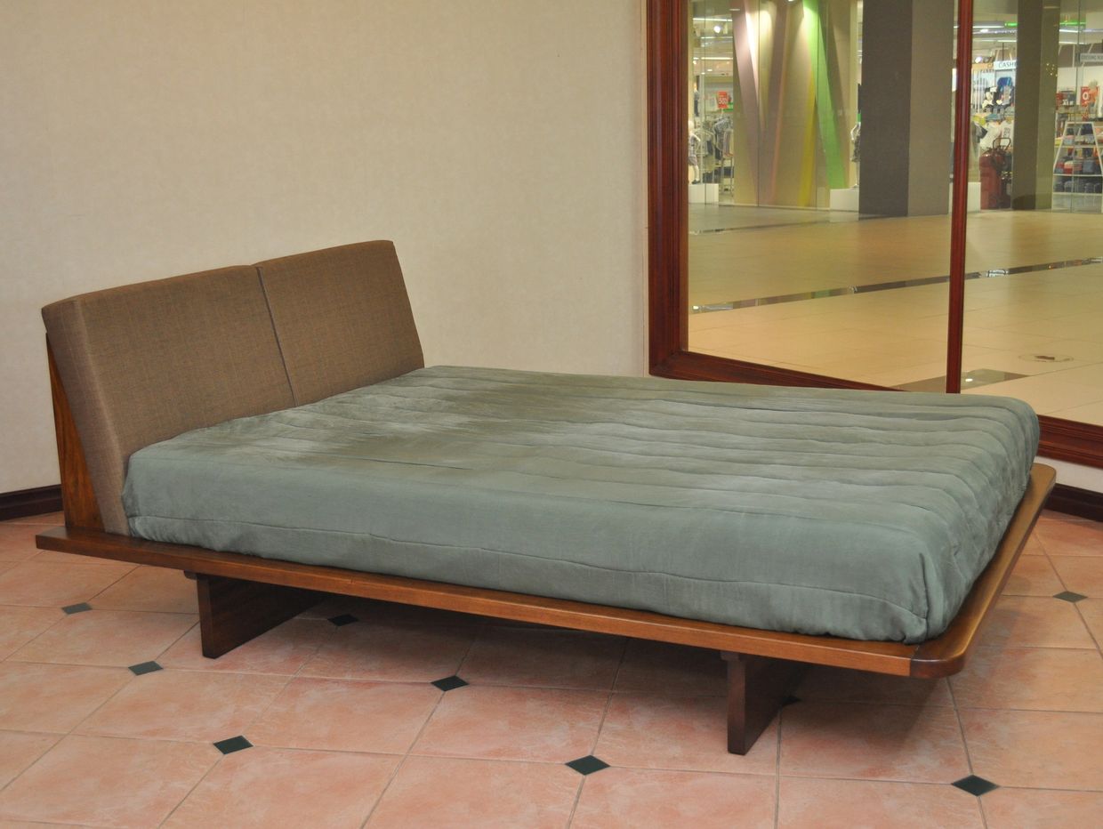 Modern wooden bed with a cushioned headboard and green bedding in a tiled room.