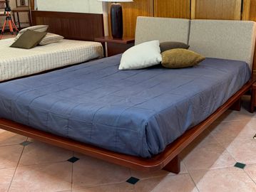 Modern wooden bed with blue bedding and decorative pillows in a showroom.