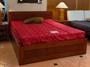 Wooden bed with red bedspread and bedside lamps in a showroom.