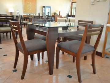 A wooden dining table with glass top and four cushioned chairs.