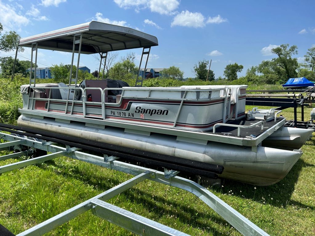 Pontoon boat parked on a trailer beside green grass.