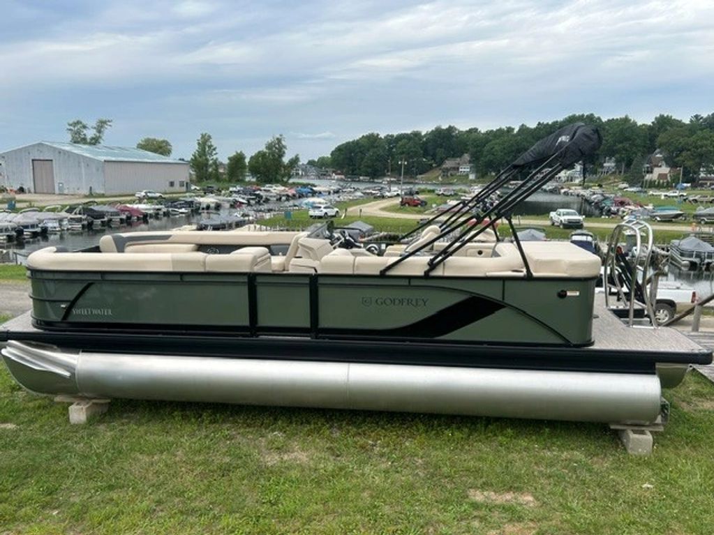 Side view of a pontoon boat on grass near a marina.