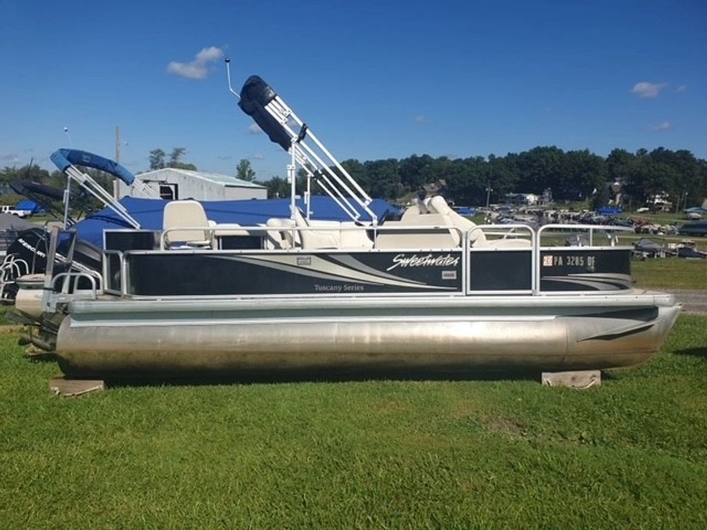 Pontoon boat parked on grass under blue sky.