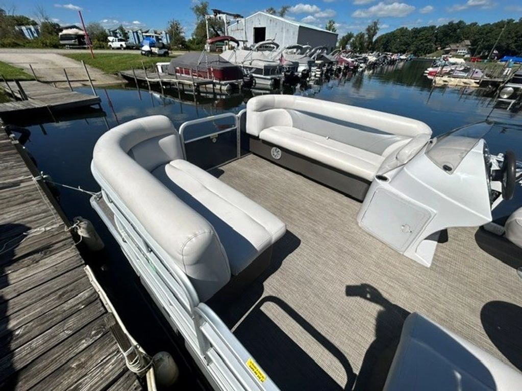 Spacious pontoon boat with white cushioned seats docked at marina.