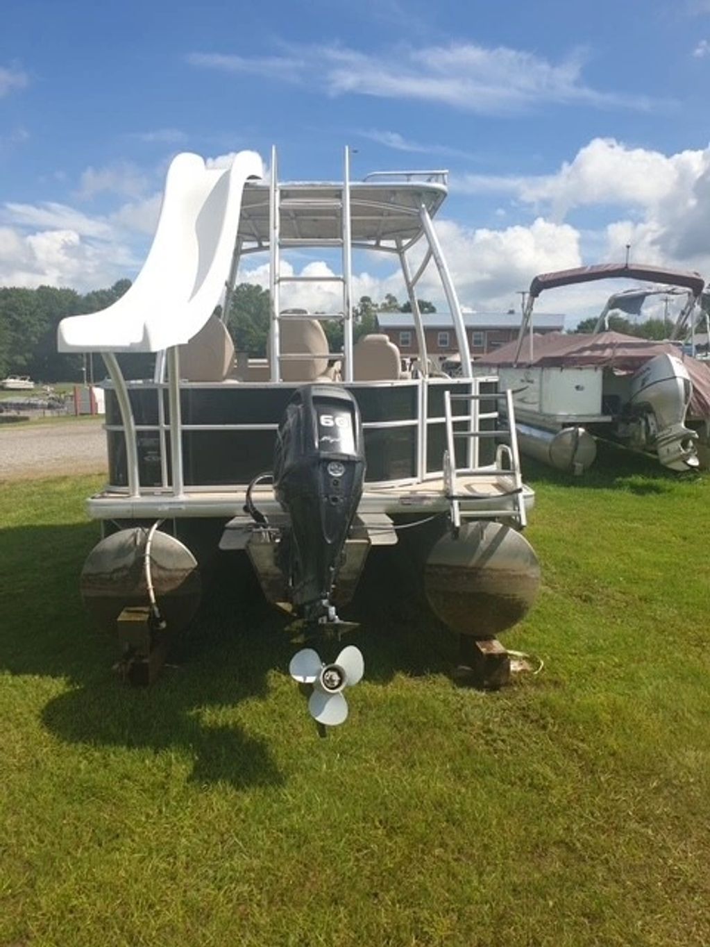 Pontoon boat with a slide on grass under blue sky.