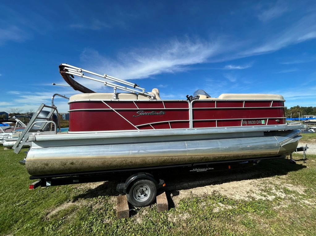 Red and silver pontoon boat on grass under a clear sky.