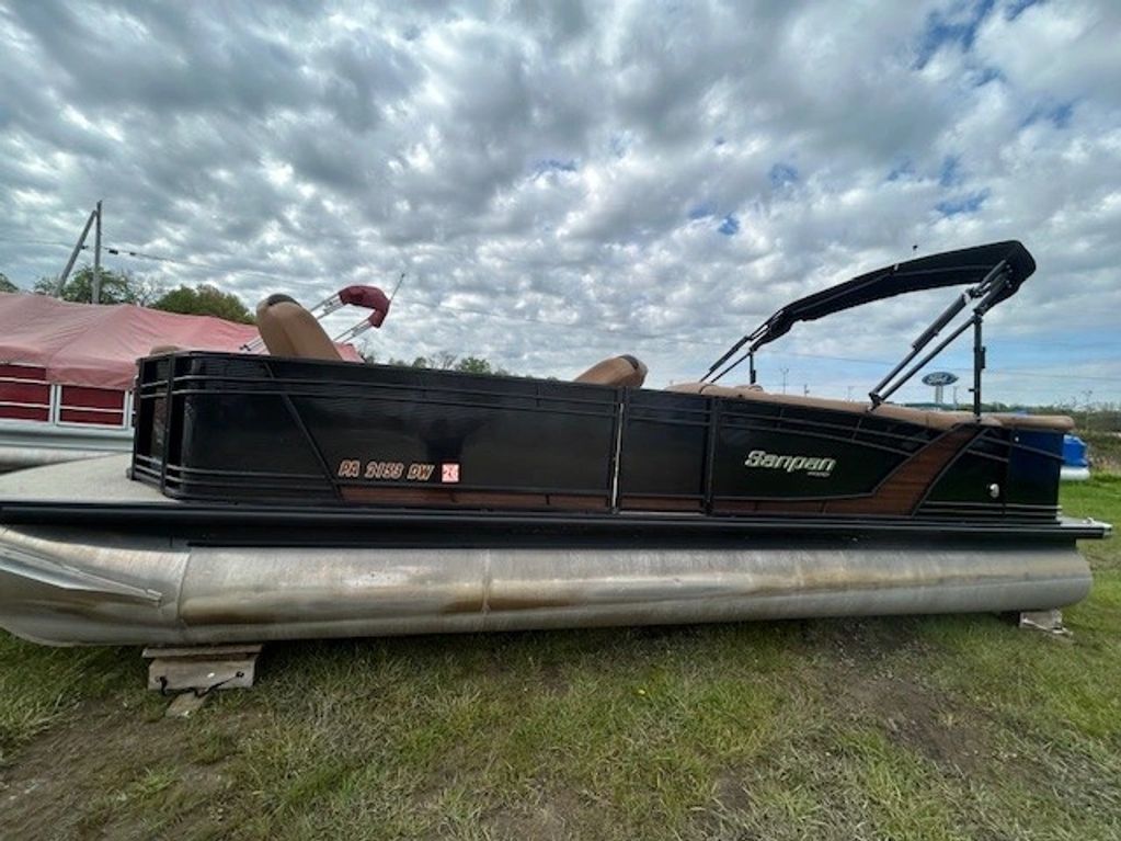 Black Sanpan pontoon boat parked on grass under a cloudy sky.