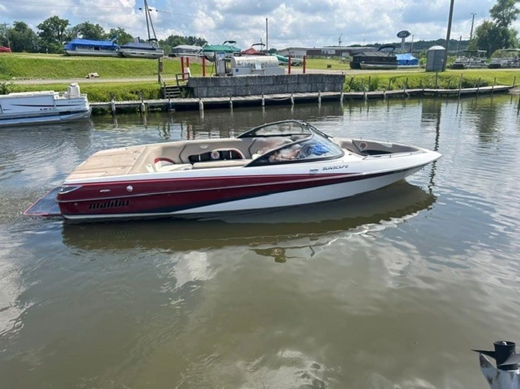 A sleek Malibu speedboat on calm water near a dock.
