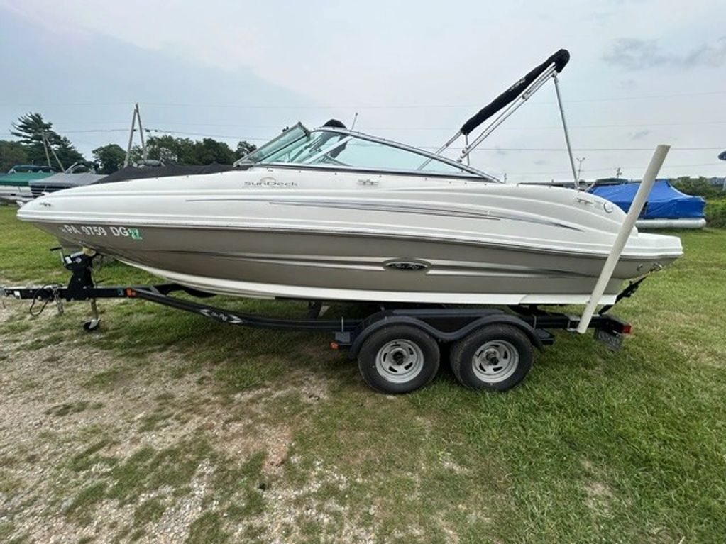 White motorboat on a black trailer in a grassy area.