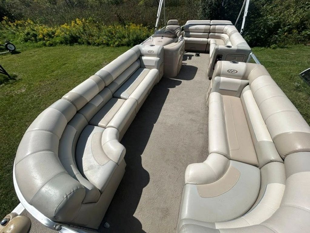 Spacious beige pontoon boat seating with outdoor greenery.