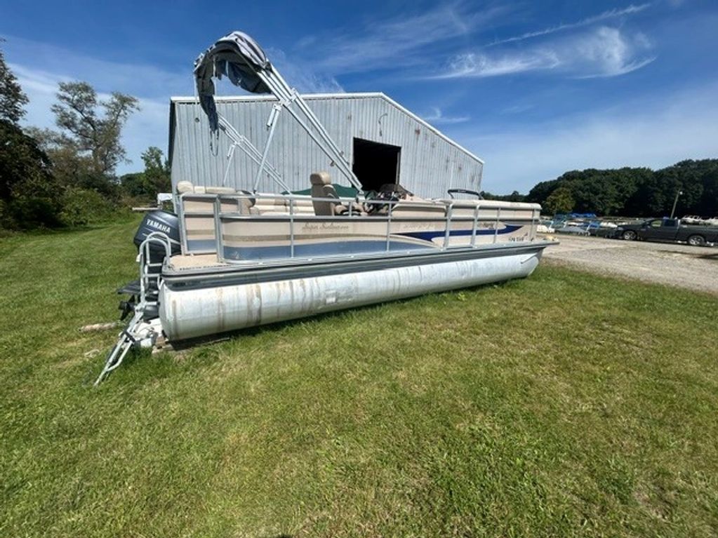 Pontoon boat parked on grass near a metal building.