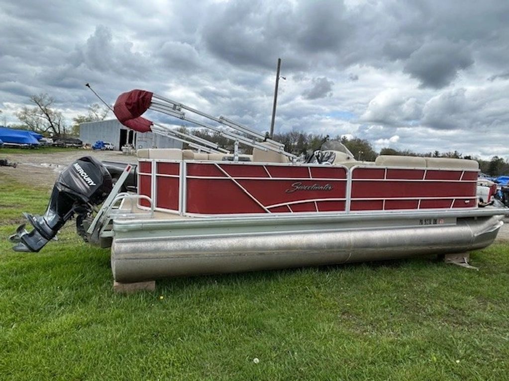Red Sweetwater pontoon boat on grass with Mercury outboard motor.
