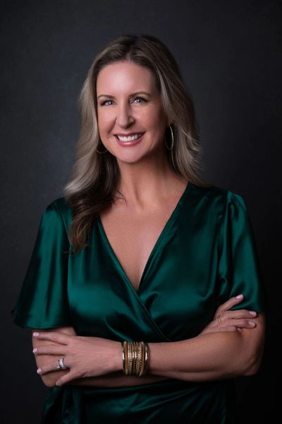 Confident woman in a green satin dress smiling with arms crossed.