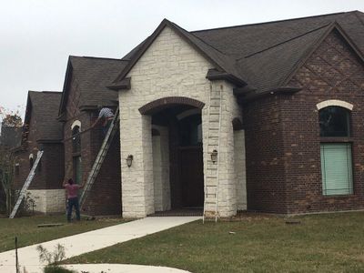 Two men working with tall ladders on the side of a brick house.