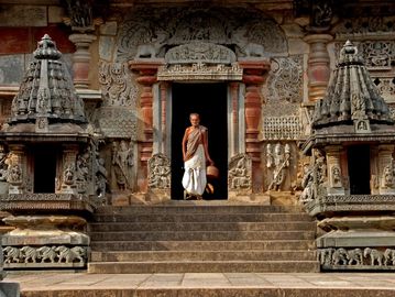 An elderly man stands at the entrance of an intricately carved ancient temple.