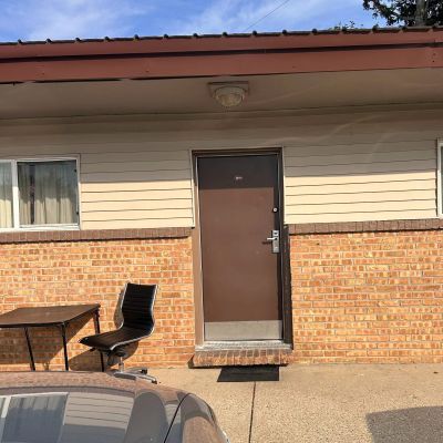 Brown door on brick building with a chair and table outside.